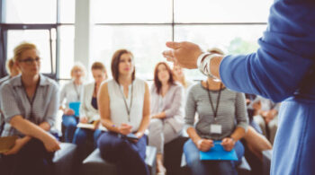 Hand of a trainer addressing group of females sitting in a conference hall. Female hand against defocused group of women attending seminar.